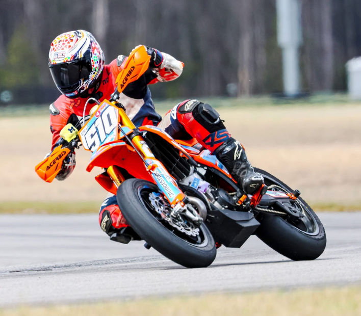 Orange motocross rider leaning hard into a turn on a racetrack, knee close to the ground.