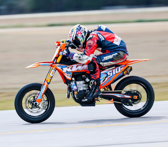 Motorcyclist in red and blue racing gear leaning into a turn on a bright orange sport bike.