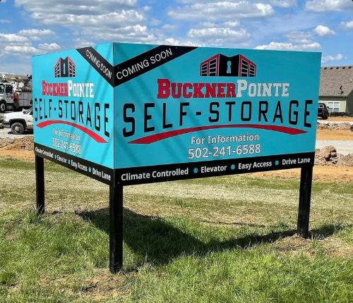 Buckner Pointe Self Storage roadside sign, teal and black, on grassy lot under cloudy sky.