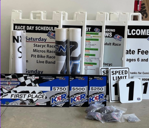 Race day table with schedule posters, prize money signs, bibs, speed limit signs, and folded shirts