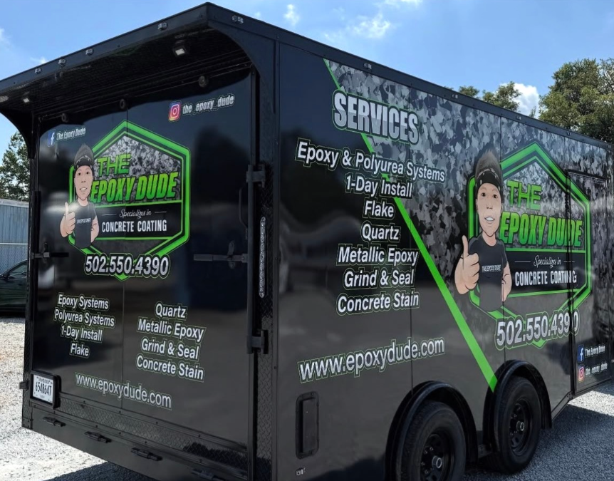 Black landscaping service trailer with green logos and a worker illustration parked outdoors.