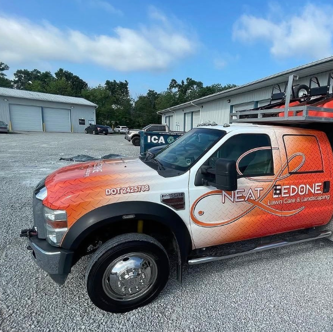 Orange and white service truck with ladder rack parked in a gravel lot near industrial buildings