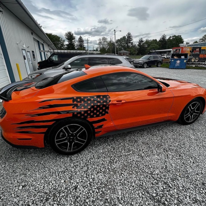 Orange sports car with black flame graphics and an American flag decal parked beside a building