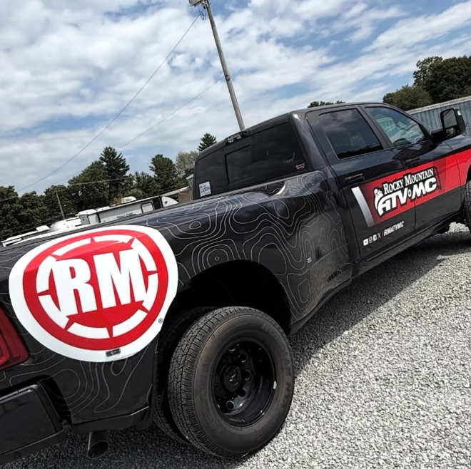 Black pickup truck with RMC graphics parked on gravel under a cloudy sky