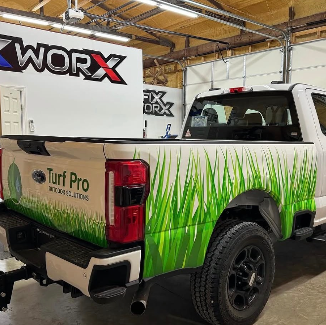Branded work truck with green grass graphics parked indoors under Worx banners