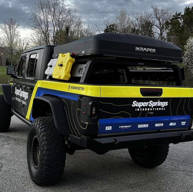 Blue and black pickup truck with yellow accents and sponsor decals, parked outdoors on a cloudy day