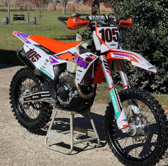 Orange and white dirt bike on a stand with number 105 in an outdoor field