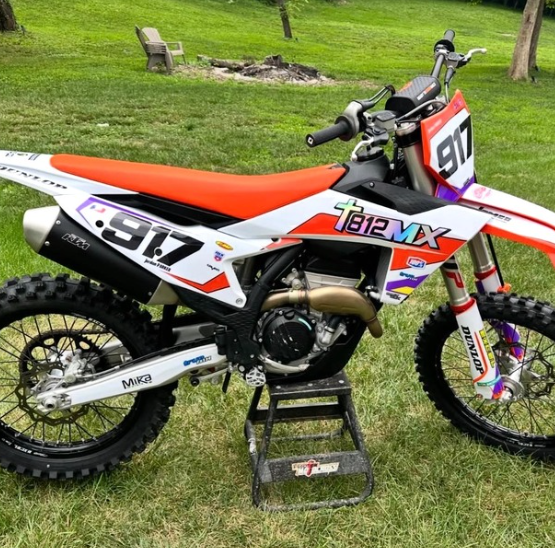 Orange-and-white dirt bike with race number 317 on a stand in a grassy outdoor area.