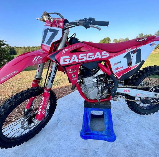 Pink GasGas dirt bike with number 17 on a stand outdoors in sunlight.