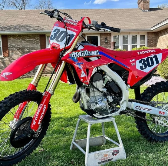 Red Honda dirt bike with number 301 on a stand in a driveway in front of a house.