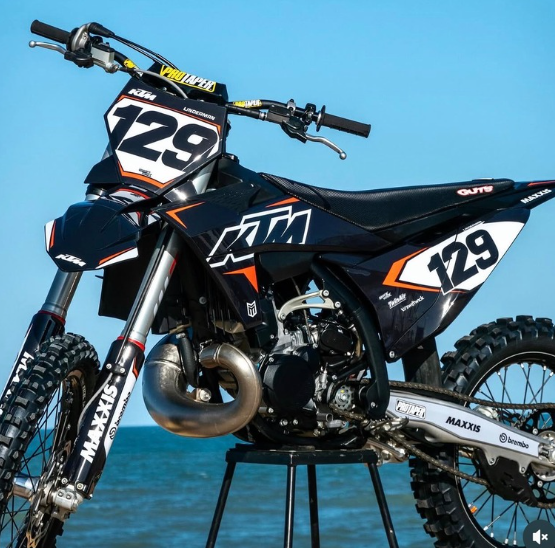 Black KTM dirt bike with number 129 on a stand against a blue sky