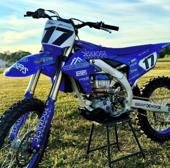 Blue motocross dirt bike with number 17 on a stand in a grassy field at sunset