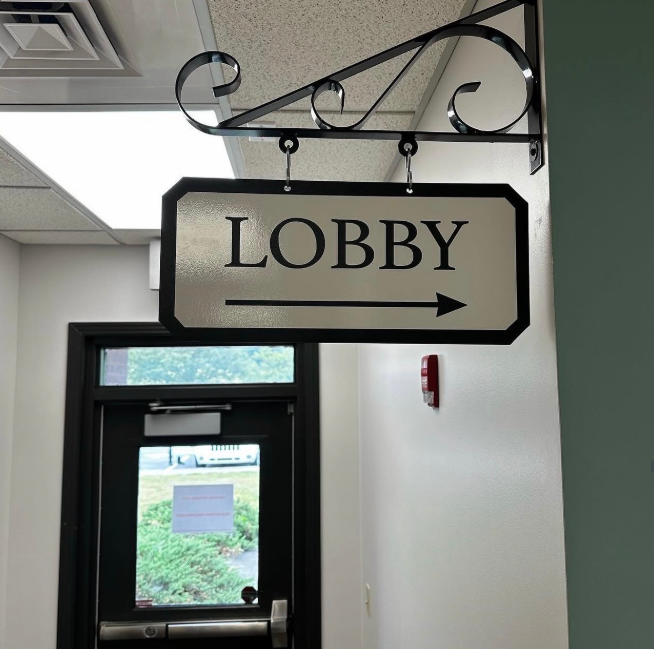 Black-and-white hanging sign reading “LOBBY” in an indoor hallway near a doorway.
