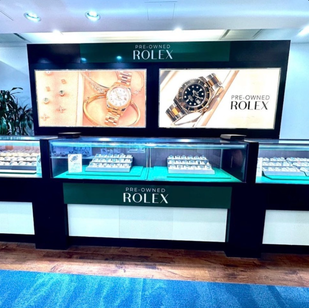 Rolex jewelry display case with watches and illuminated product ads in a store