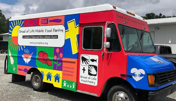 Colorful mobile food pantry truck parked outdoors, with red cab and bright food bank graphics.