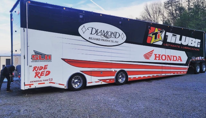 White Honda race transport trailer with Diamond and Tilube logos parked outdoors on gravel.