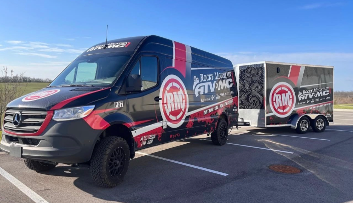 Red-and-black RTM service truck and matching trailer parked in a sunny lot under a blue sky