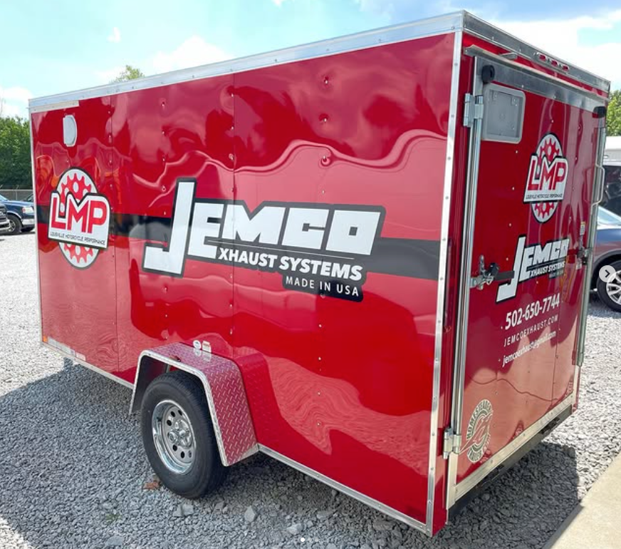 Red enclosed trailer with JEMCO Exhaust Systems logo parked on gravel lot
