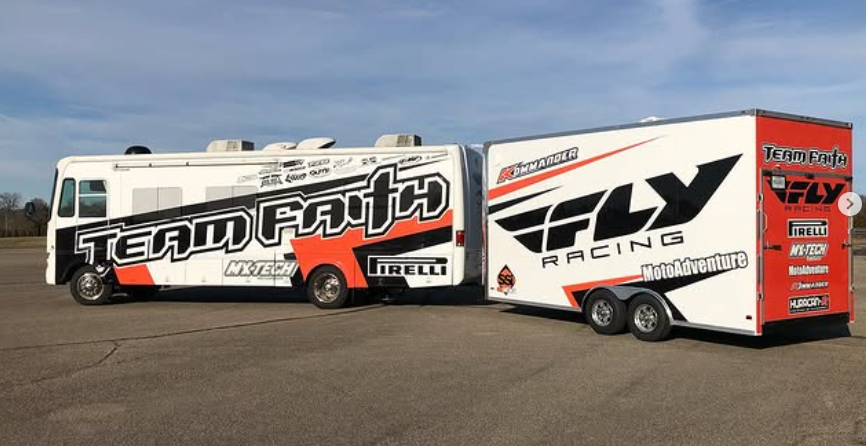 Two Team Faith racing transport trucks parked side by side on a lot, white and red with bold logos