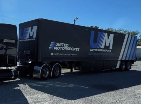 Black United Motorsports trailer with large blue-and-white UM logo parked outdoors under a clear sky