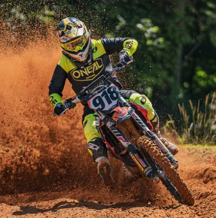 Motocross rider in yellow gear leans into a muddy turn, spraying orange dirt