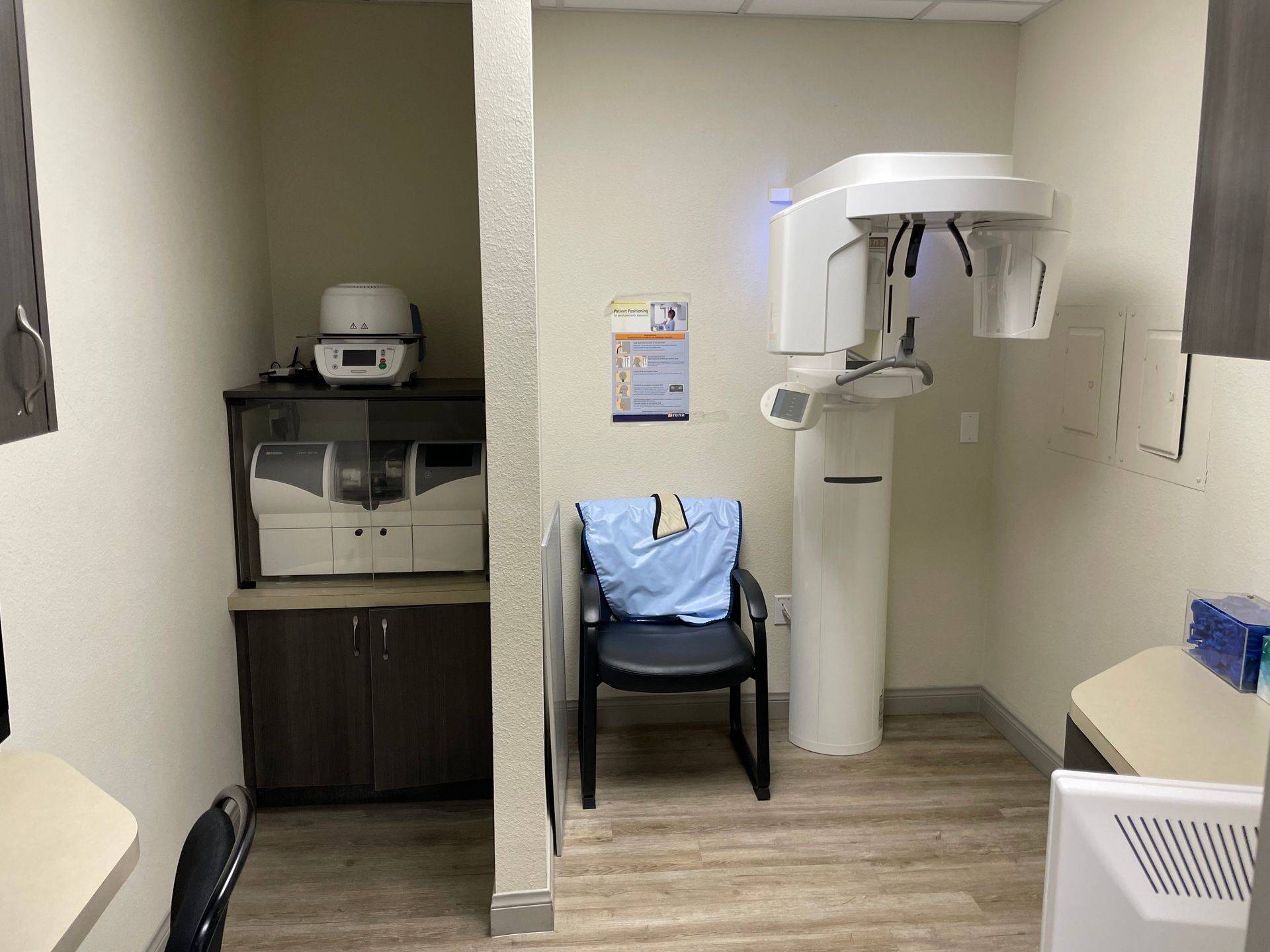 Medical exam room with dental imaging machine, chair, sink, and cabinet in a beige clinic office.