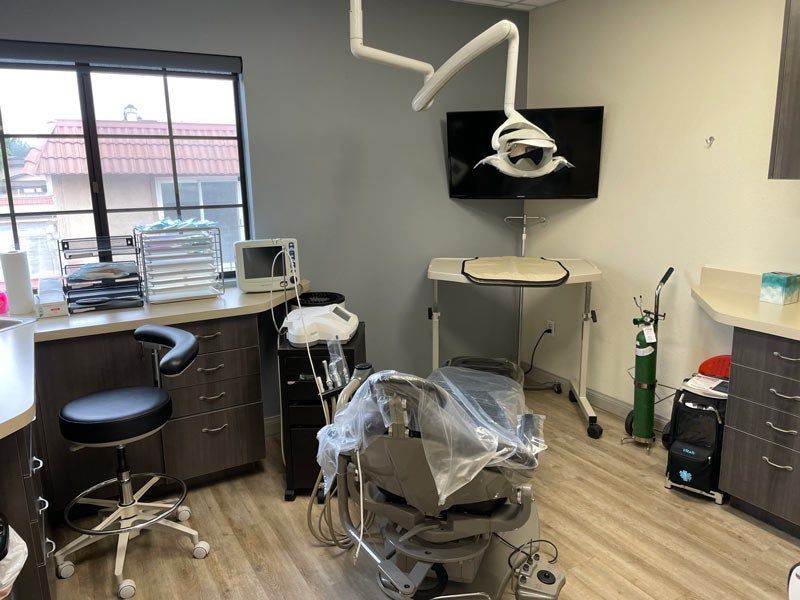 Dental treatment room with chair, overhead light, stools, and cabinets by a window