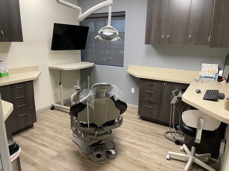 Empty dental treatment room with chair, overhead light, cabinets, and computer monitors