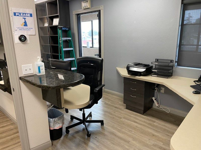Office reception area with desk, chair, computer printer, and glass door in a gray room
