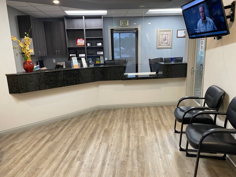 Empty lobby with front desk, black chairs, wall TV, and wood-look flooring.