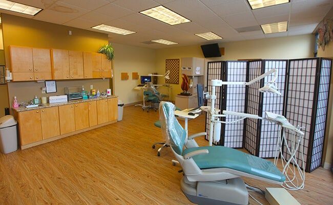 Dental office with turquoise chairs, wooden cabinets, and a treatment area behind folding screens