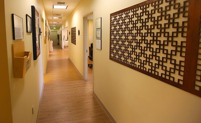 Empty hallway with wooden floor, beige walls, framed art, and overhead lights