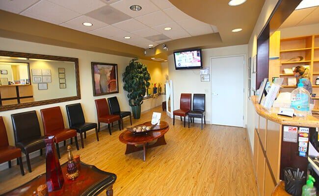 Bright dental waiting room with wooden floors, red chairs, TV, and reception counter