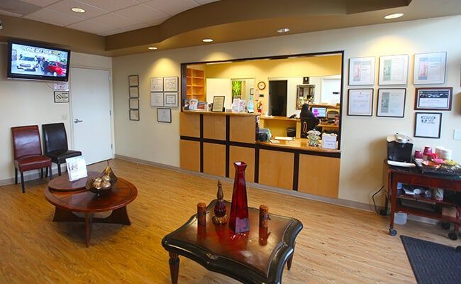 Bright waiting room with reception desk, chairs, wooden floors, and framed certificates on the wall
