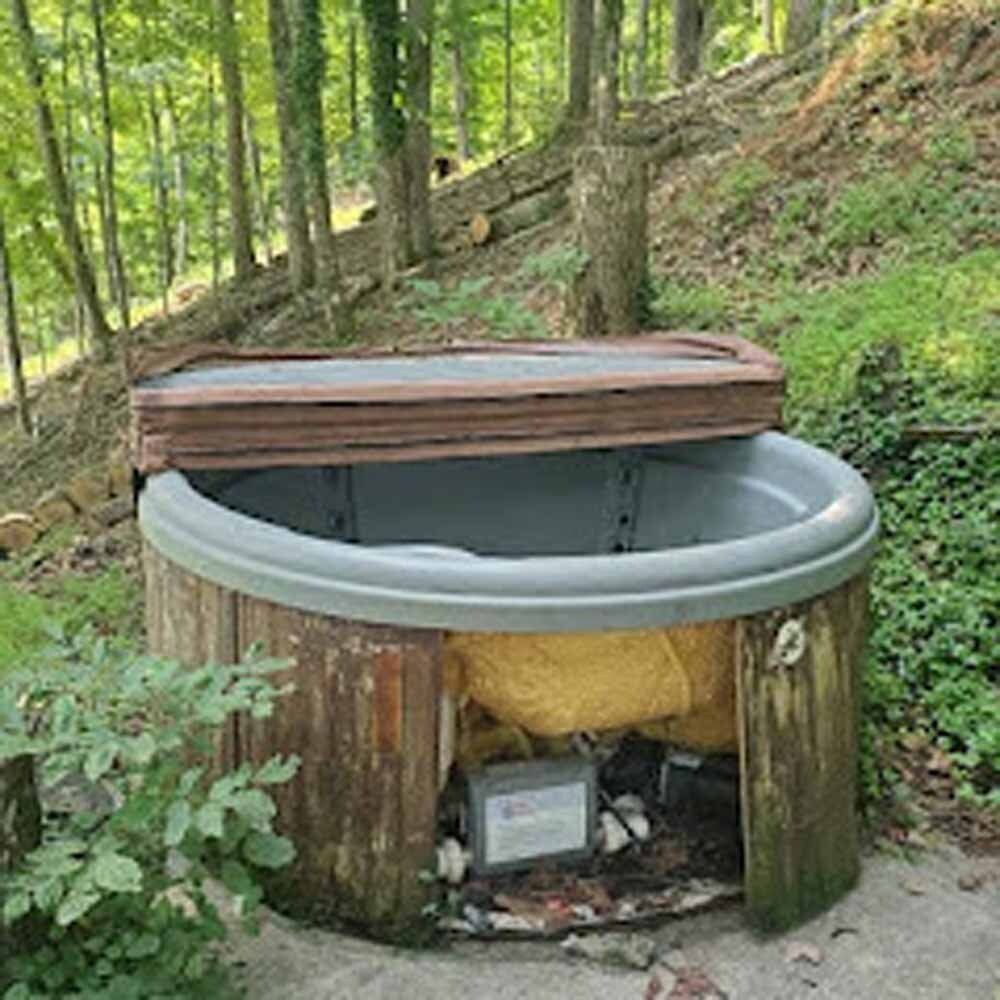 Outdoor hot tub or barrel spa with a wooden lid in a wooded hillside setting