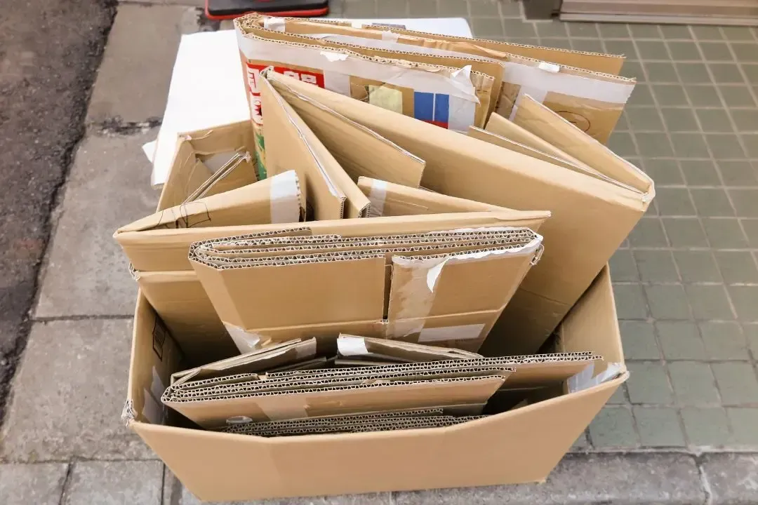 A pile of cardboard boxes are stacked on top of each other on the sidewalk.