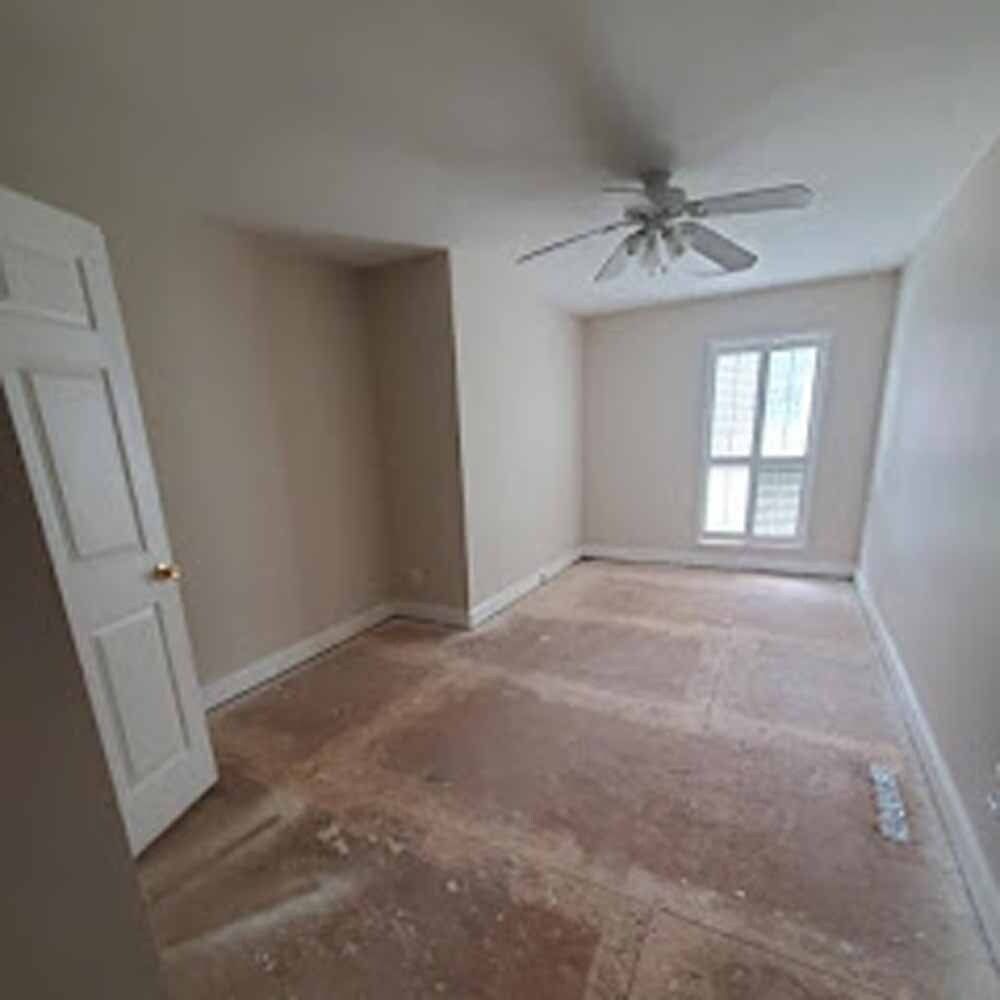 Empty beige bedroom with carpet being removed, ceiling fan, and window with blinds.