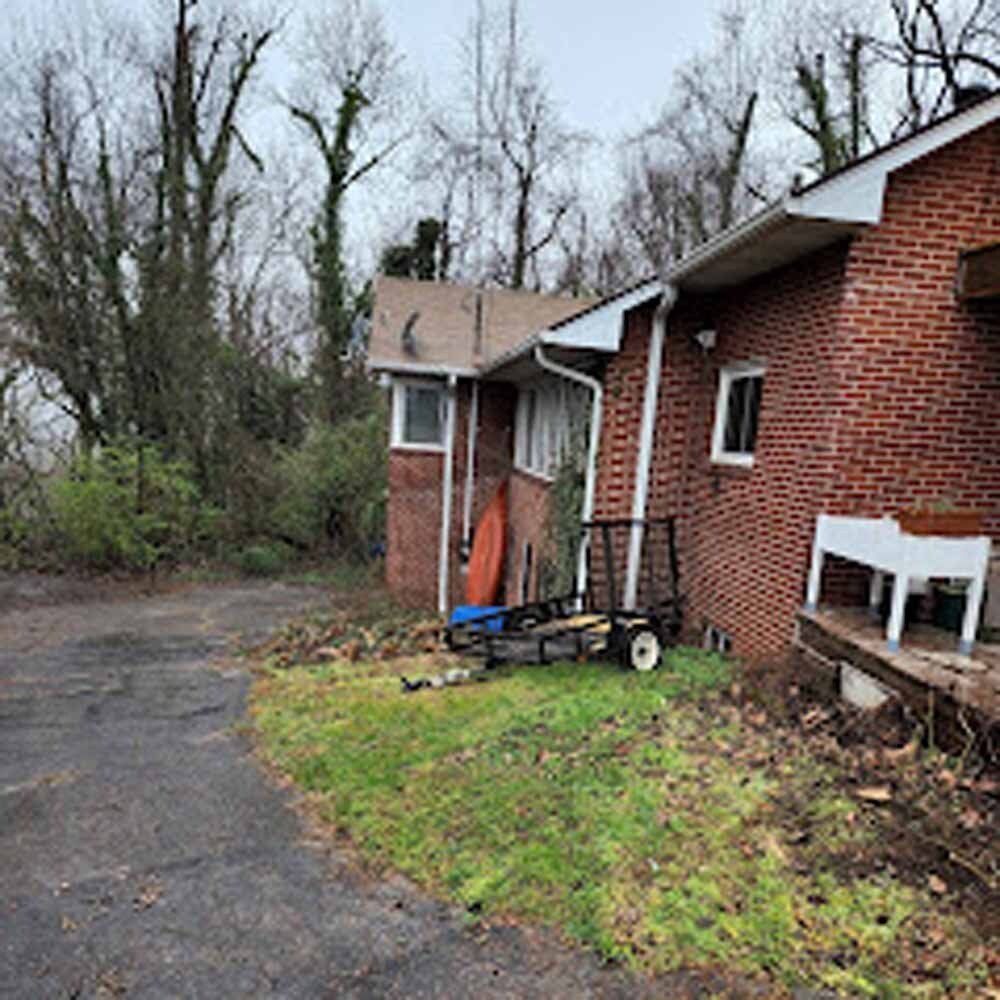Brick house exterior with wet driveway, overcast sky, and a small cart by the porch