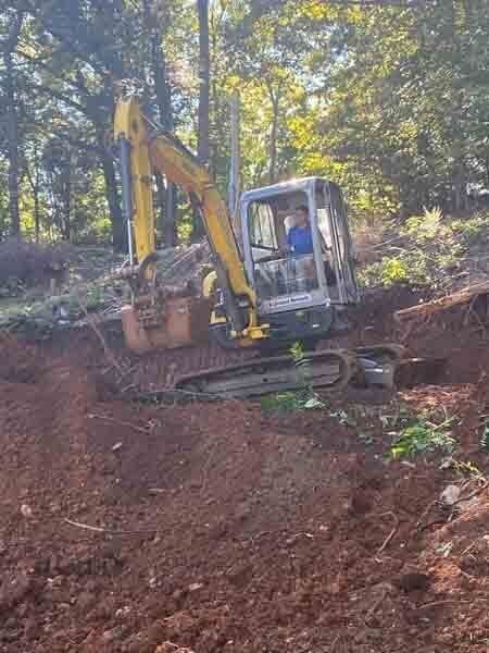 Yellow excavator working on a steep dirt slope in a wooded area
