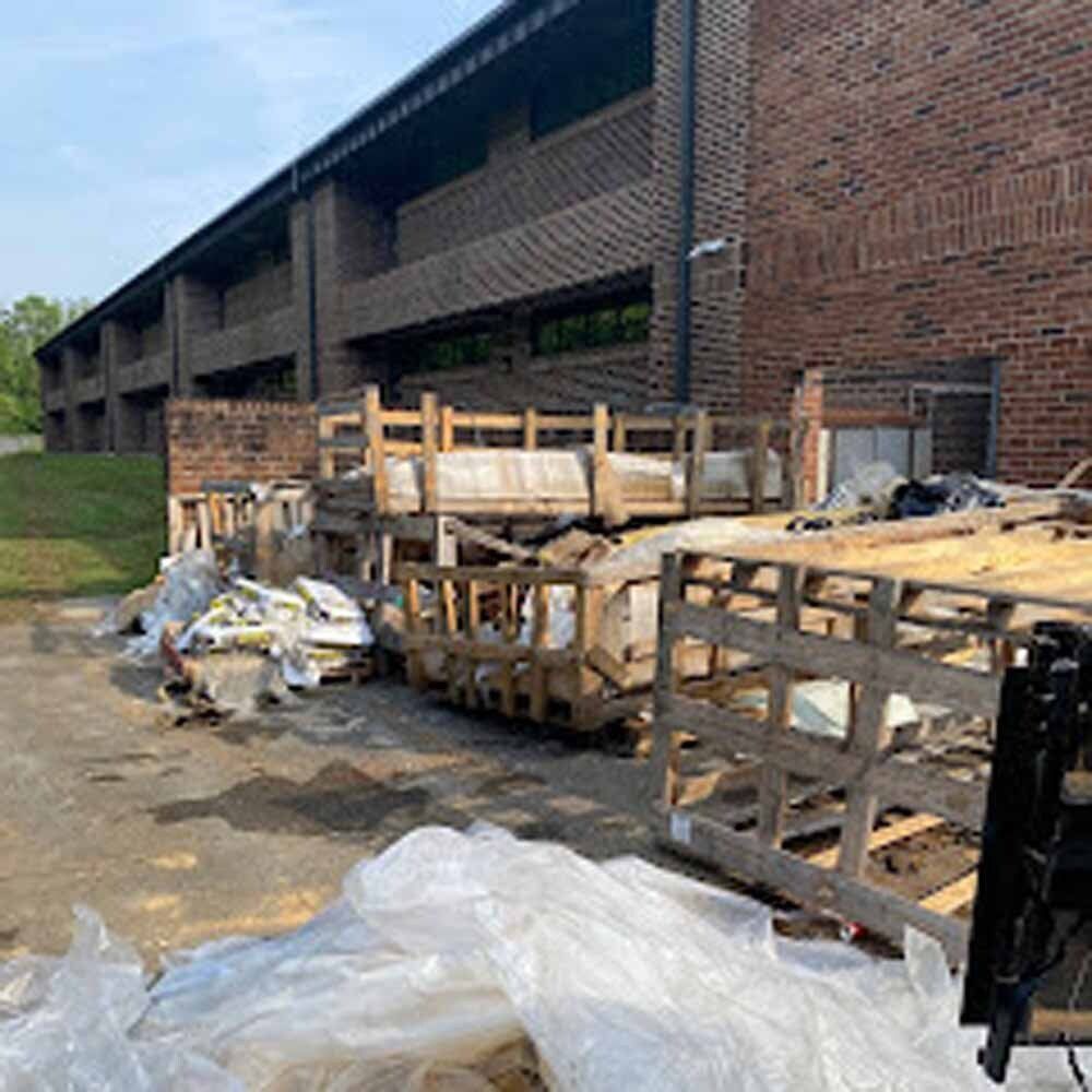 Pallets of trash and debris piled beside a brick building on a wet concrete lot