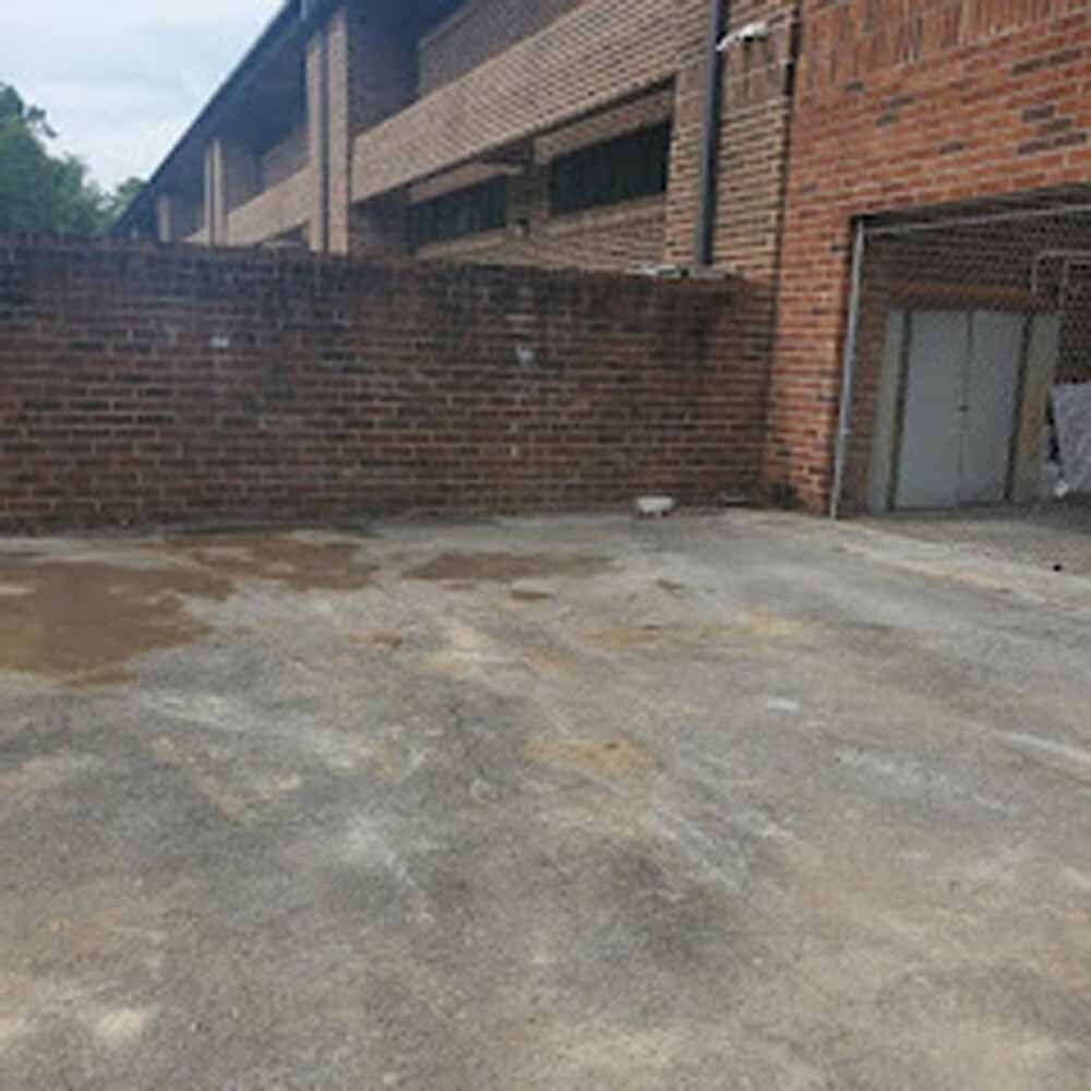 Empty concrete courtyard beside a brick building and wall, with a small metal doorway on the right.