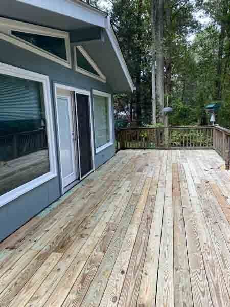 Wooden deck beside a blue house with large windows, surrounded by trees and a railing.