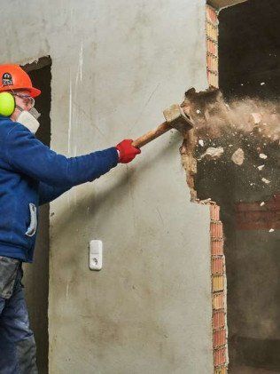 Worker in red hard hat demolishing a wall with a sledgehammer inside a room