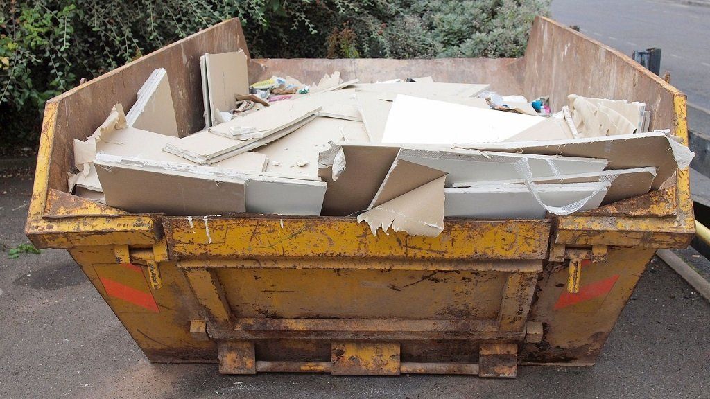 Yellow dumpster filled with broken white furniture and debris outdoors