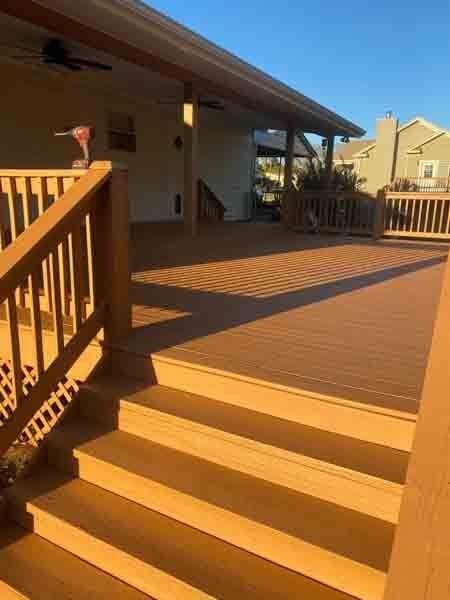 Wooden deck with steps and railing in warm sunlight beside a house