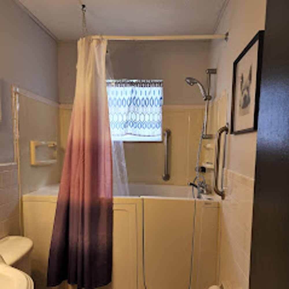 Bathroom with a bathtub, purple shower curtain, showerhead, and small frosted window