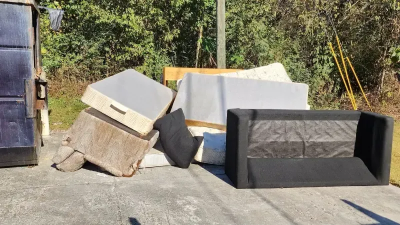 A pile of furniture is sitting on the ground next to a dumpster.