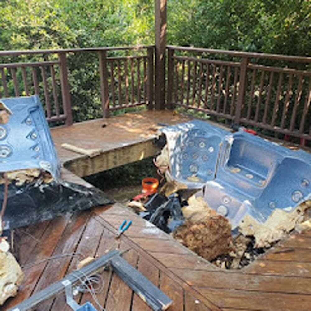 Burned hot tub with melted blue seats on a wooden deck, surrounded by trees
