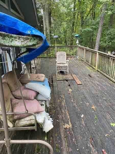 Wooden deck in a wooded backyard with a swing chair, cushions, and a blue tarp overhead