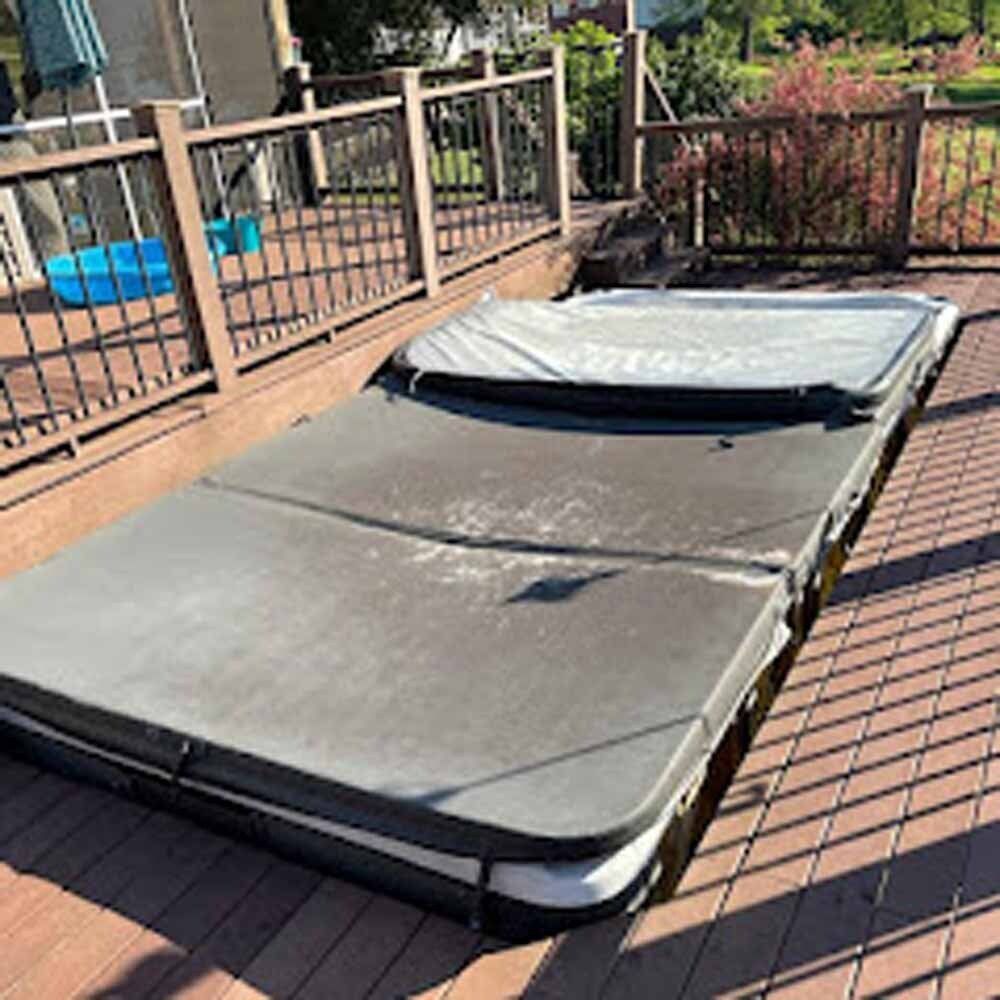 Folded gray mattress or cushion on a wooden deck beside a railing and pool.